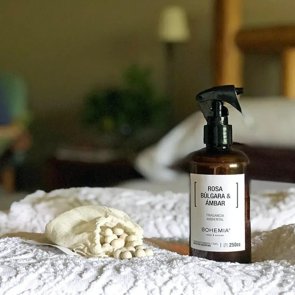 Botella de spray marrón y bolsa de cuentas beige sobre una superficie texturizada blanca, posiblemente una cama.