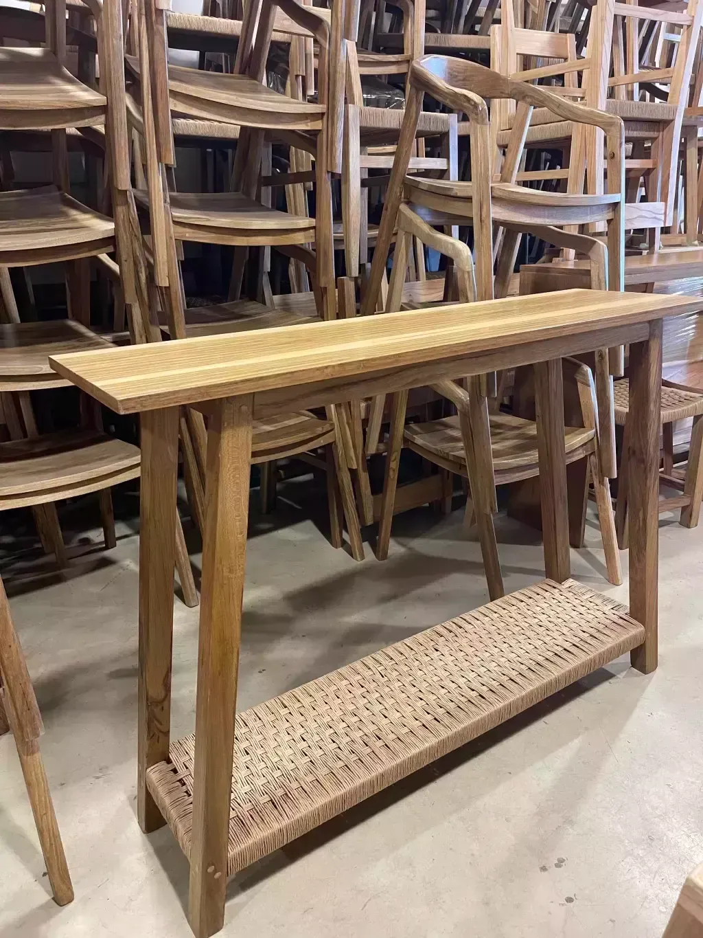 Consola de madera con estante tejido, rodeada de sillas de madera en un taller.
