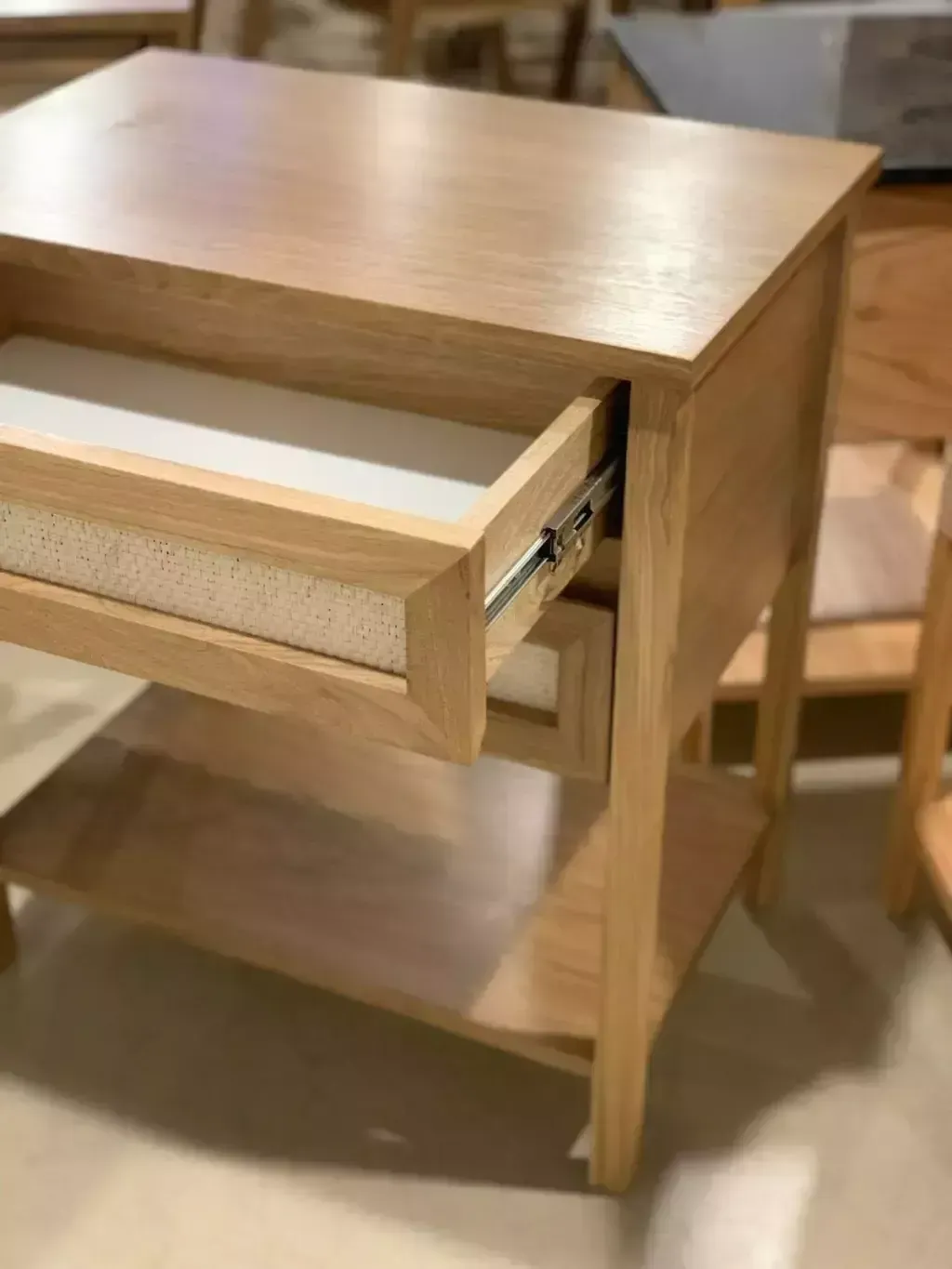 Mesita de noche de madera clara con dos cajones, estante y tapa cuadrada.