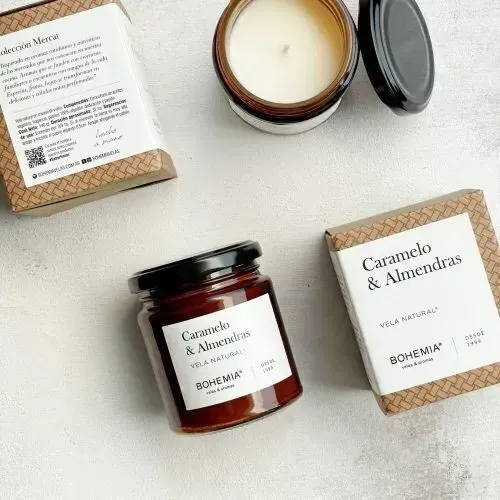 Fotografía cenital de dos velas y un tarro de caramelo y mermelada de almendras sobre una superficie blanca.