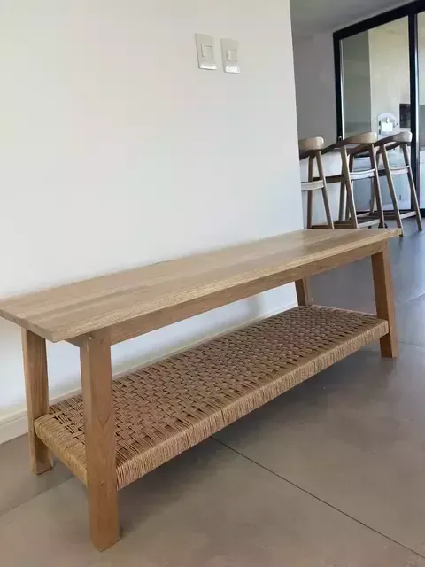 Banco de madera con estante tejido, contra una pared blanca.