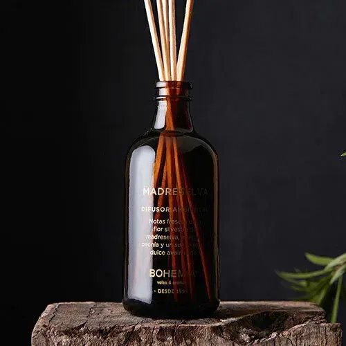 Botella difusora de vidrio ámbar con juncos, rodajas de pomelo y virutas de madera sobre una superficie de madera.