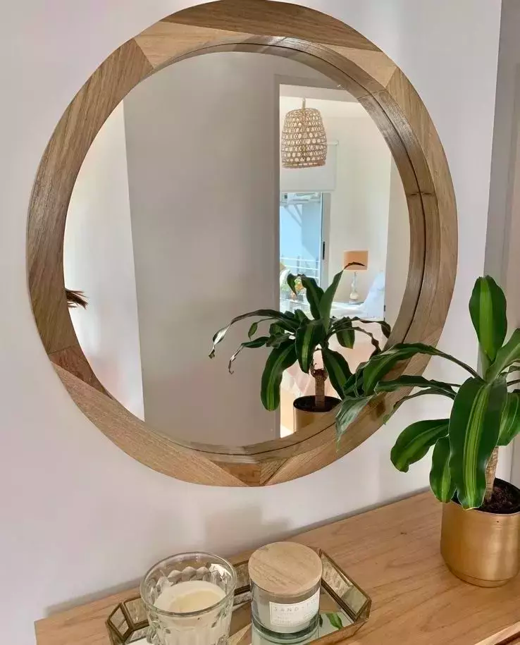 Espejo redondo con marco de madera colgado sobre una mesa de madera, con plantas y velas.