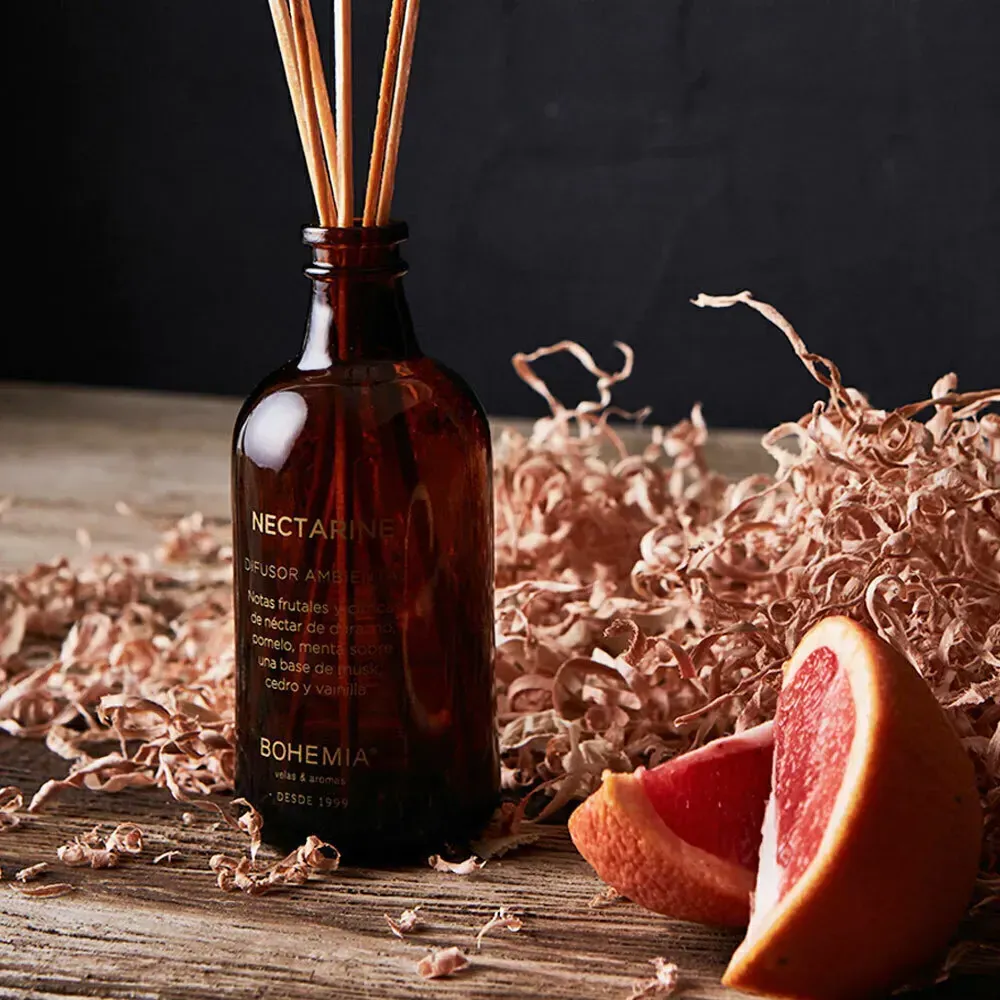 Botella difusora de vidrio ámbar con juncos, rodajas de pomelo y virutas de madera sobre una superficie de madera.
