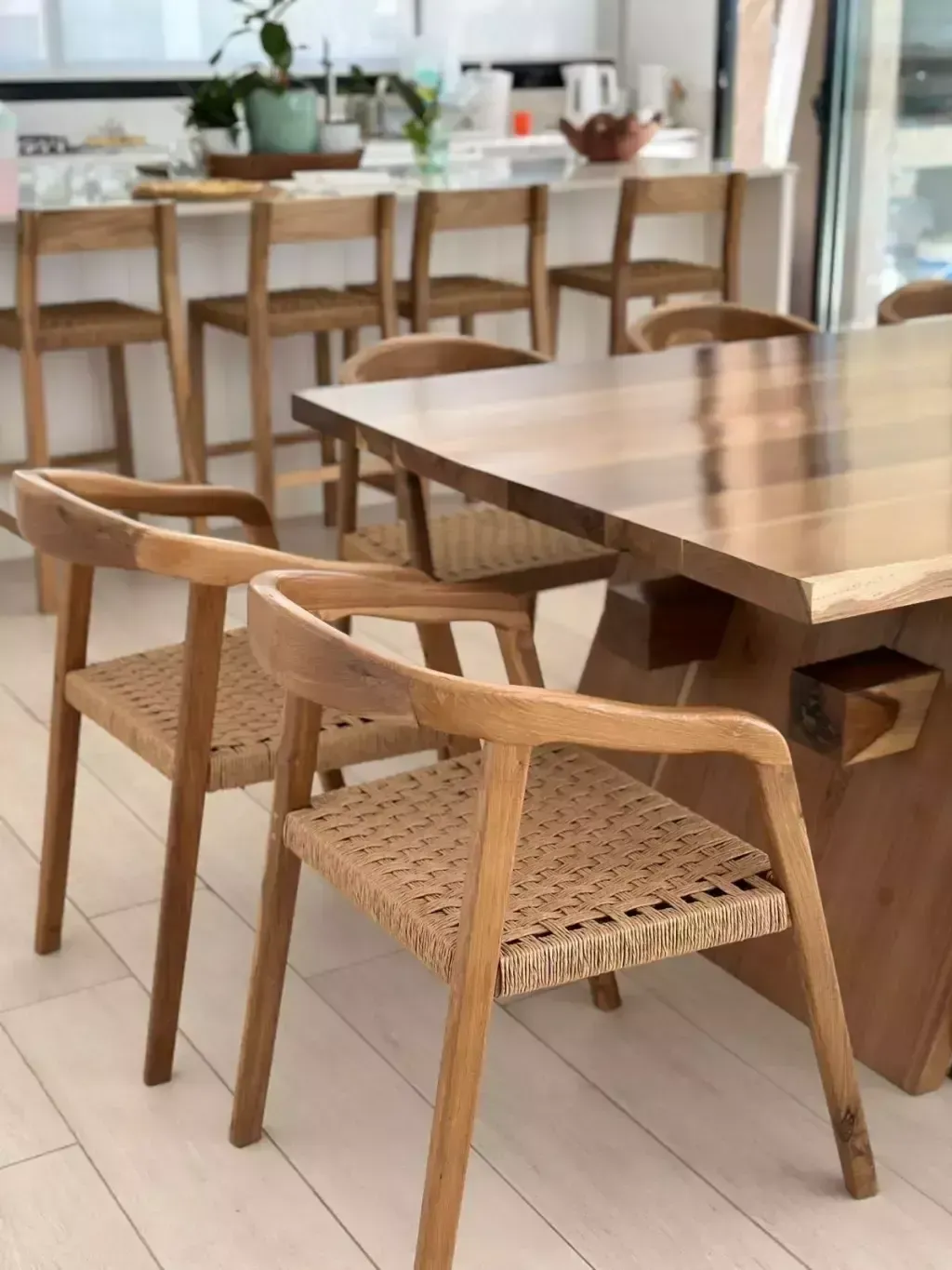 Mesa de comedor de madera y sillas con asientos tejidos en un ambiente de cocina luminoso.