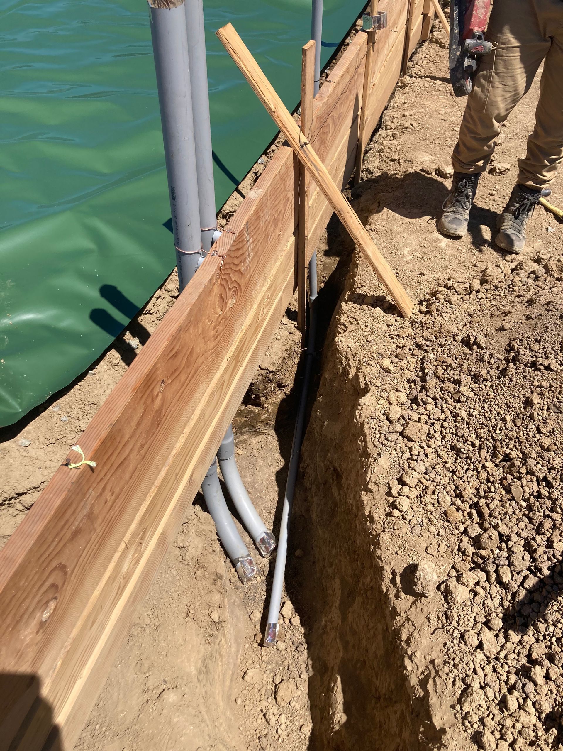 A man is standing in the dirt next to a wooden fence.