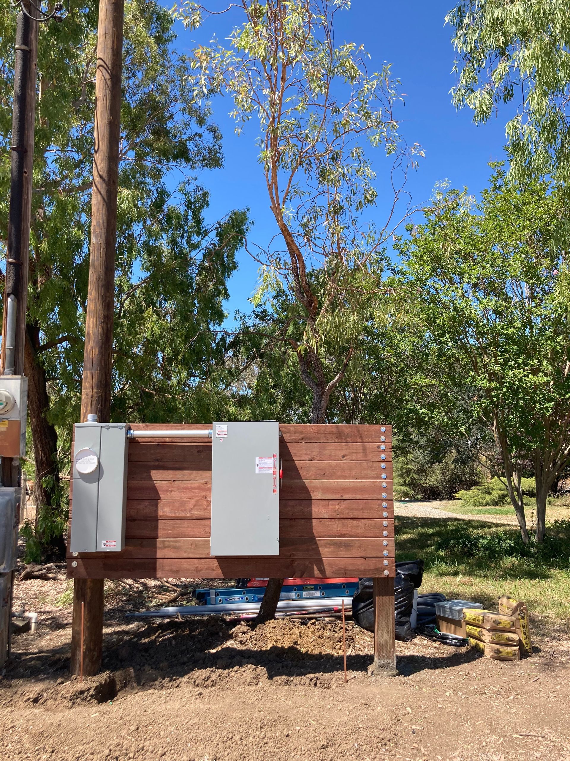 A wooden box is sitting on top of a dirt field next to a tree.