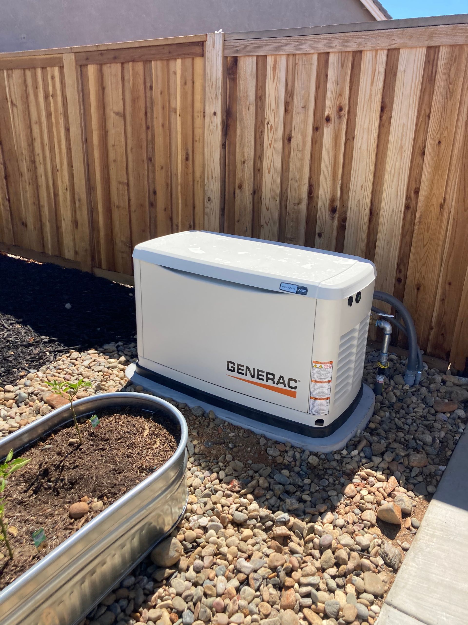 A generator is sitting on top of a pile of rocks next to a wooden fence.