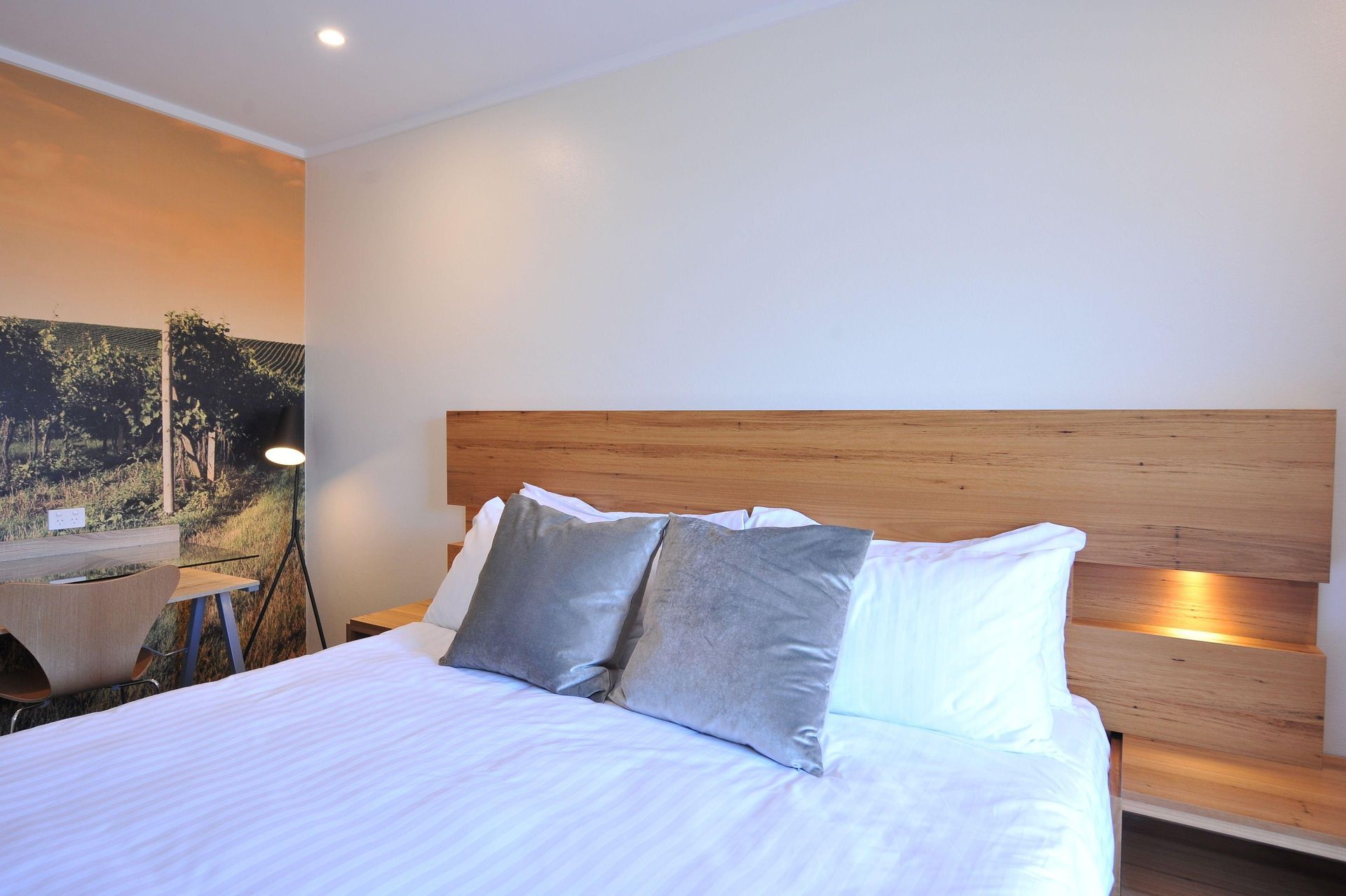 Bright bedroom with a large white bed and wood headboard, beside a small balcony seating area