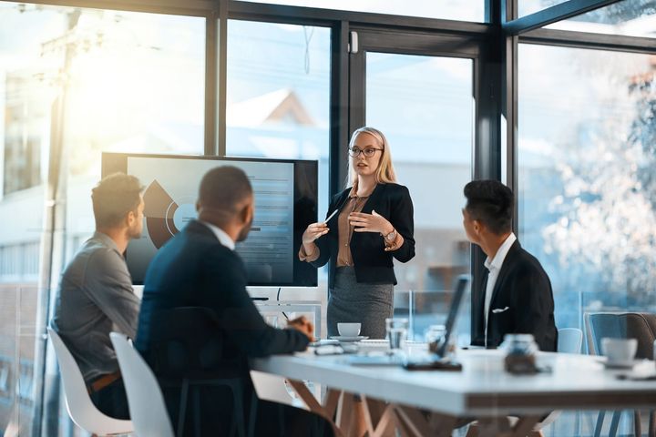 A woman is giving a presentation to a group of business people in a conference room.