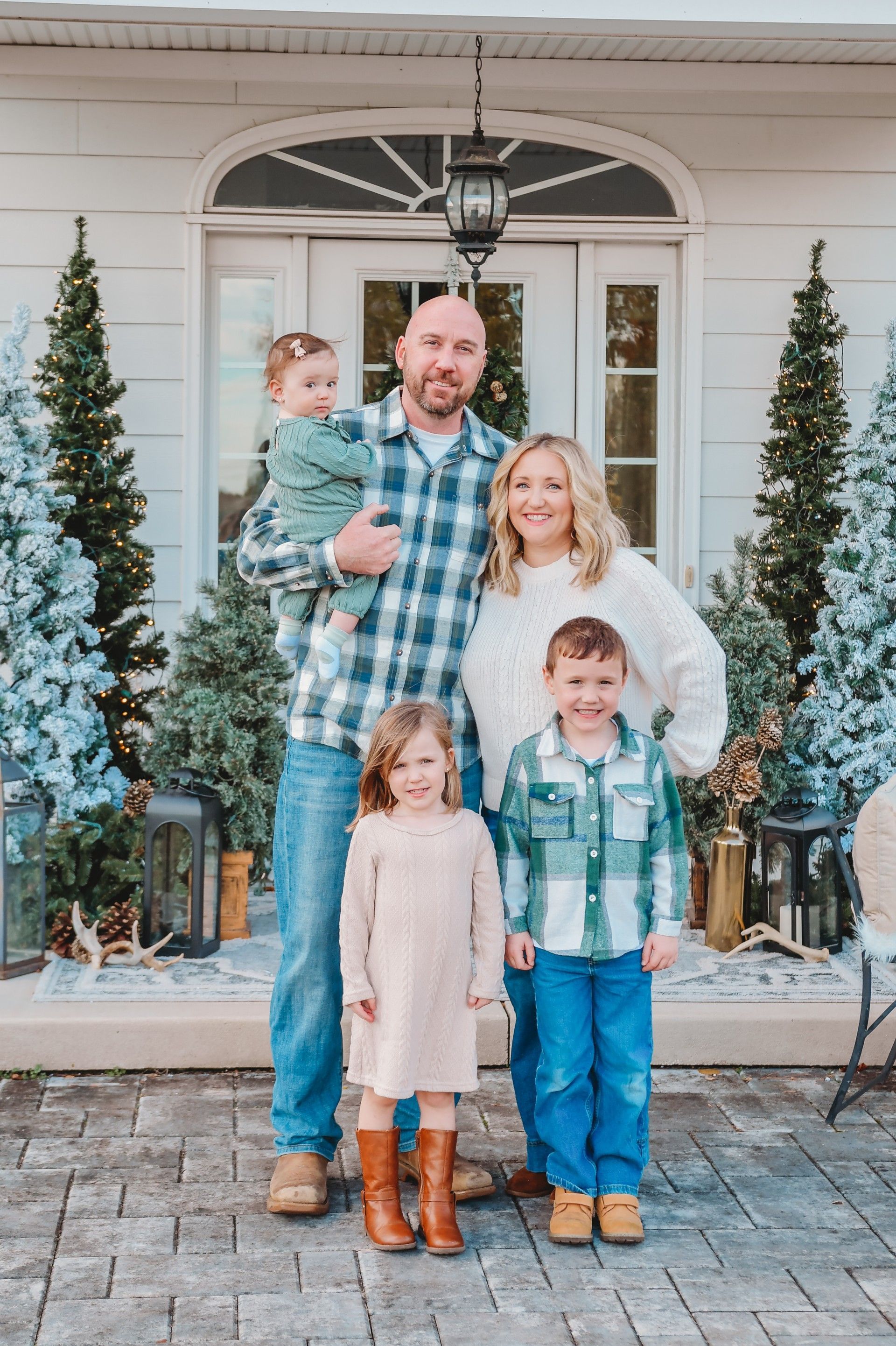 A family of five posing in front of a house with two small trees, decorated for the holidays.