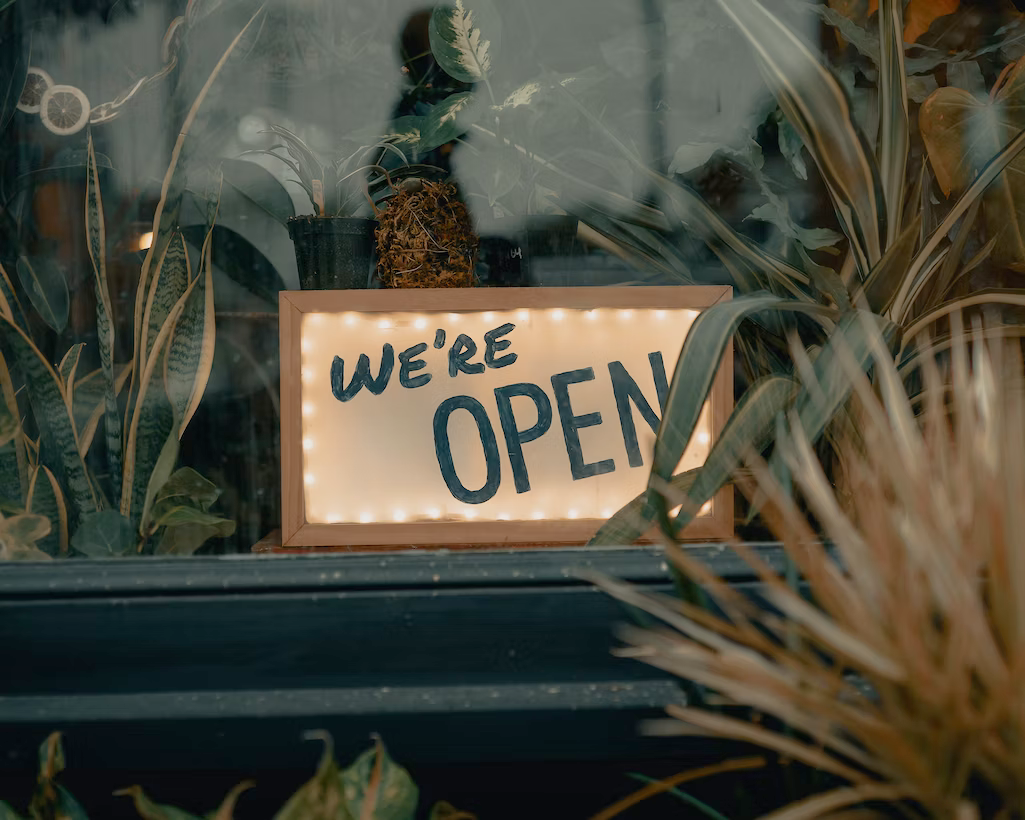 A sign that says `` we 're open '' is in a window surrounded by plants.