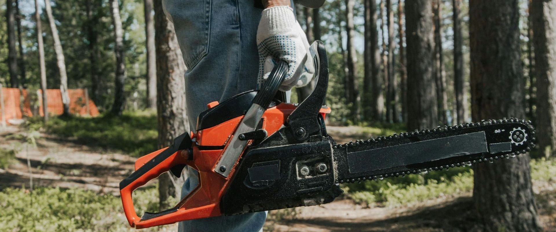 a close up of a man's hand holding a chainsaw in a forest.