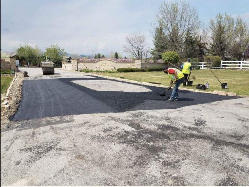 A man is laying asphalt on the side of a road.