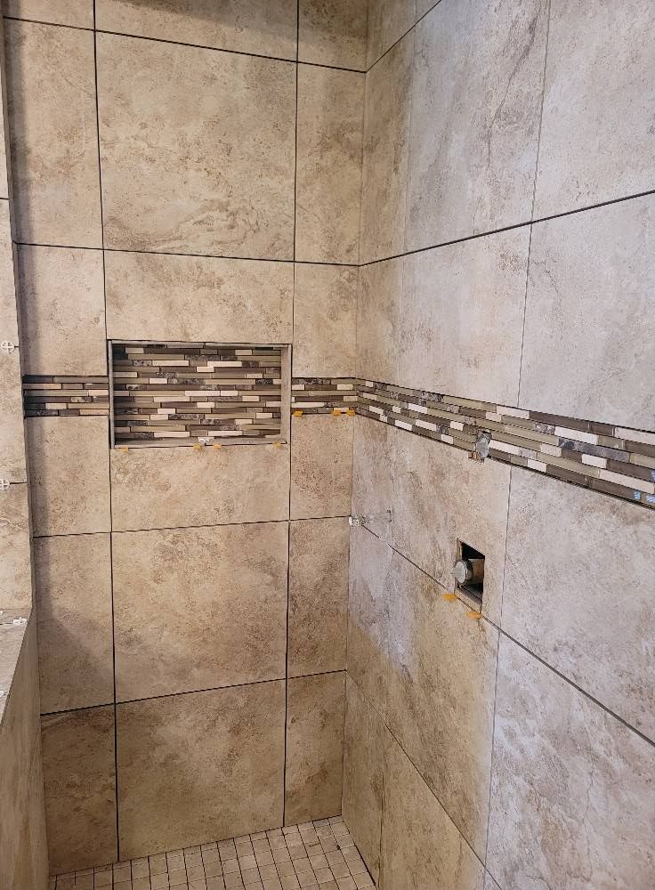 A shower with tiled walls and a shelf in the corner.