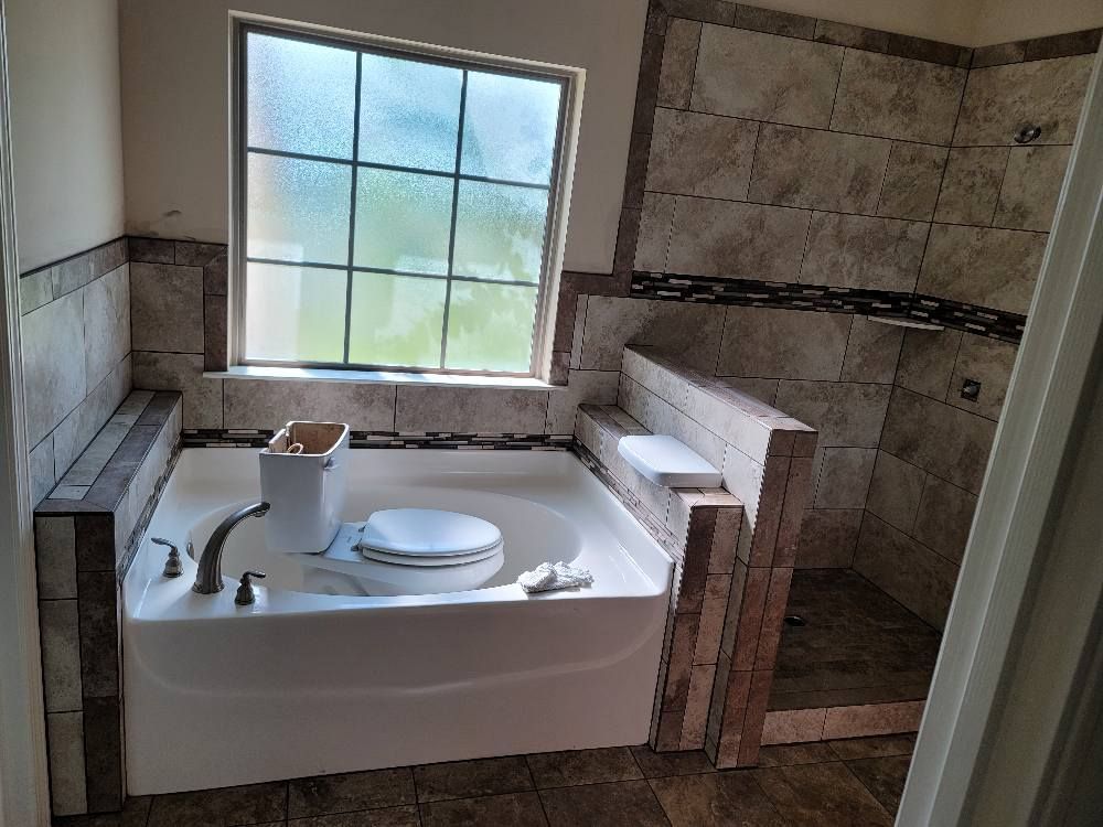 A bathroom with a tub , toilet , shower and window.