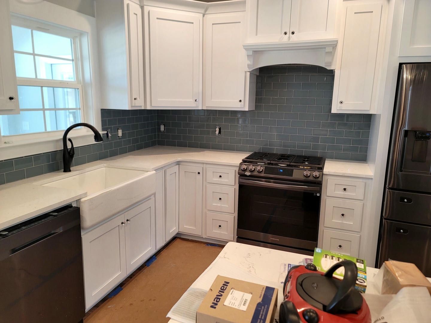 A kitchen with white cabinets , a stove , a sink , and a vacuum cleaner.