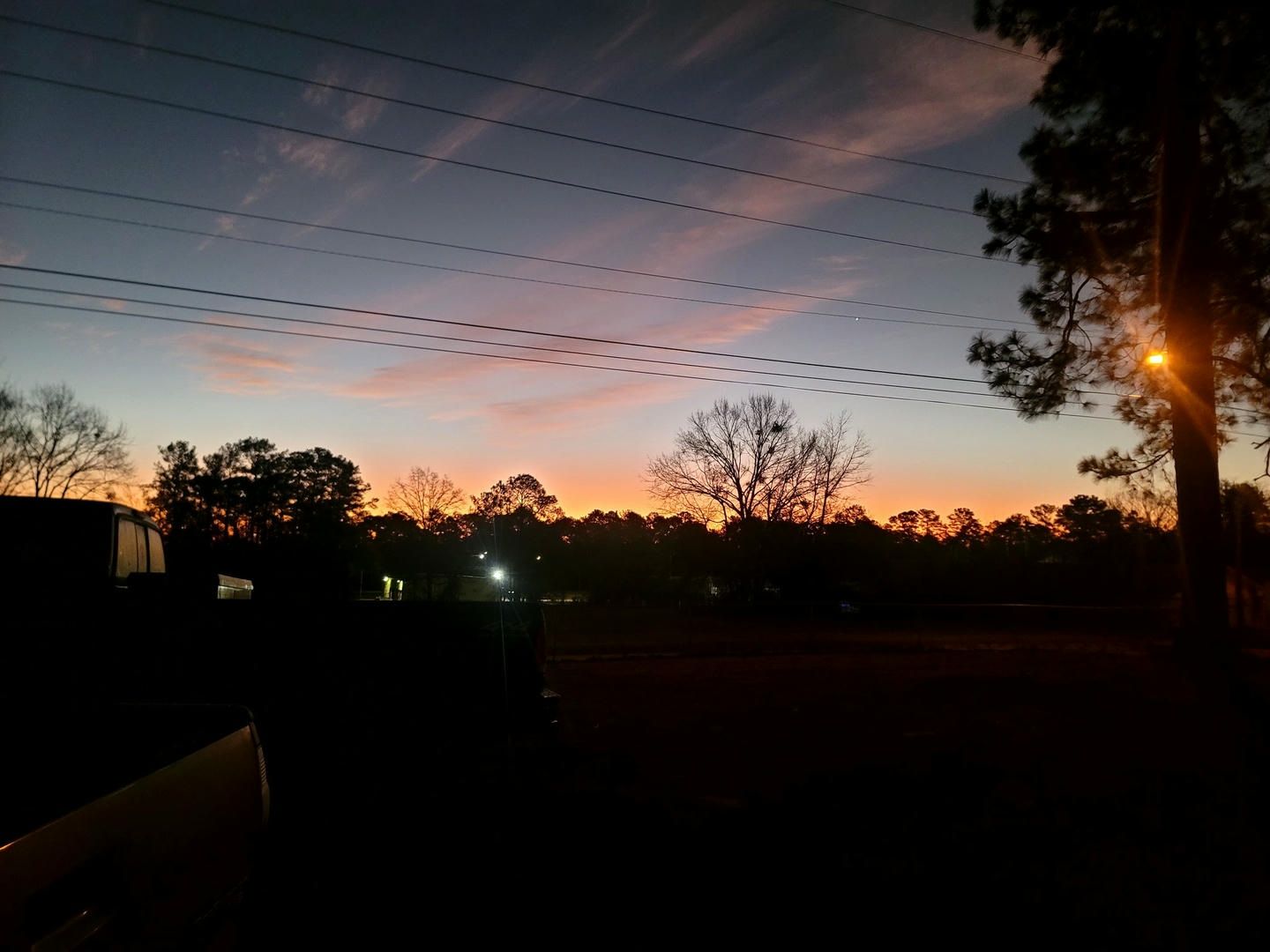 A sunset with trees and power lines in the foreground