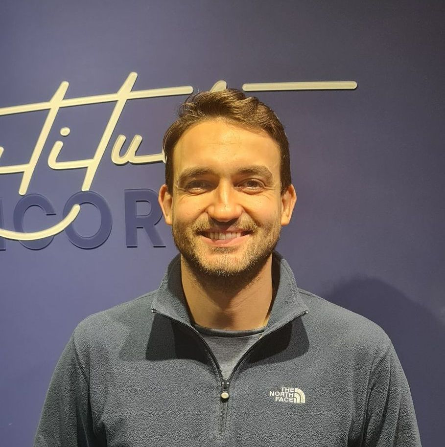 Um homem barbudo sorri para a câmera em frente a uma janela.