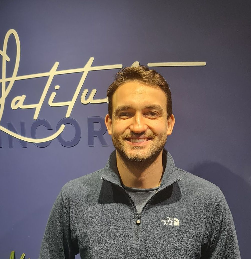 Um homem barbudo sorri para a câmera em frente a uma janela.