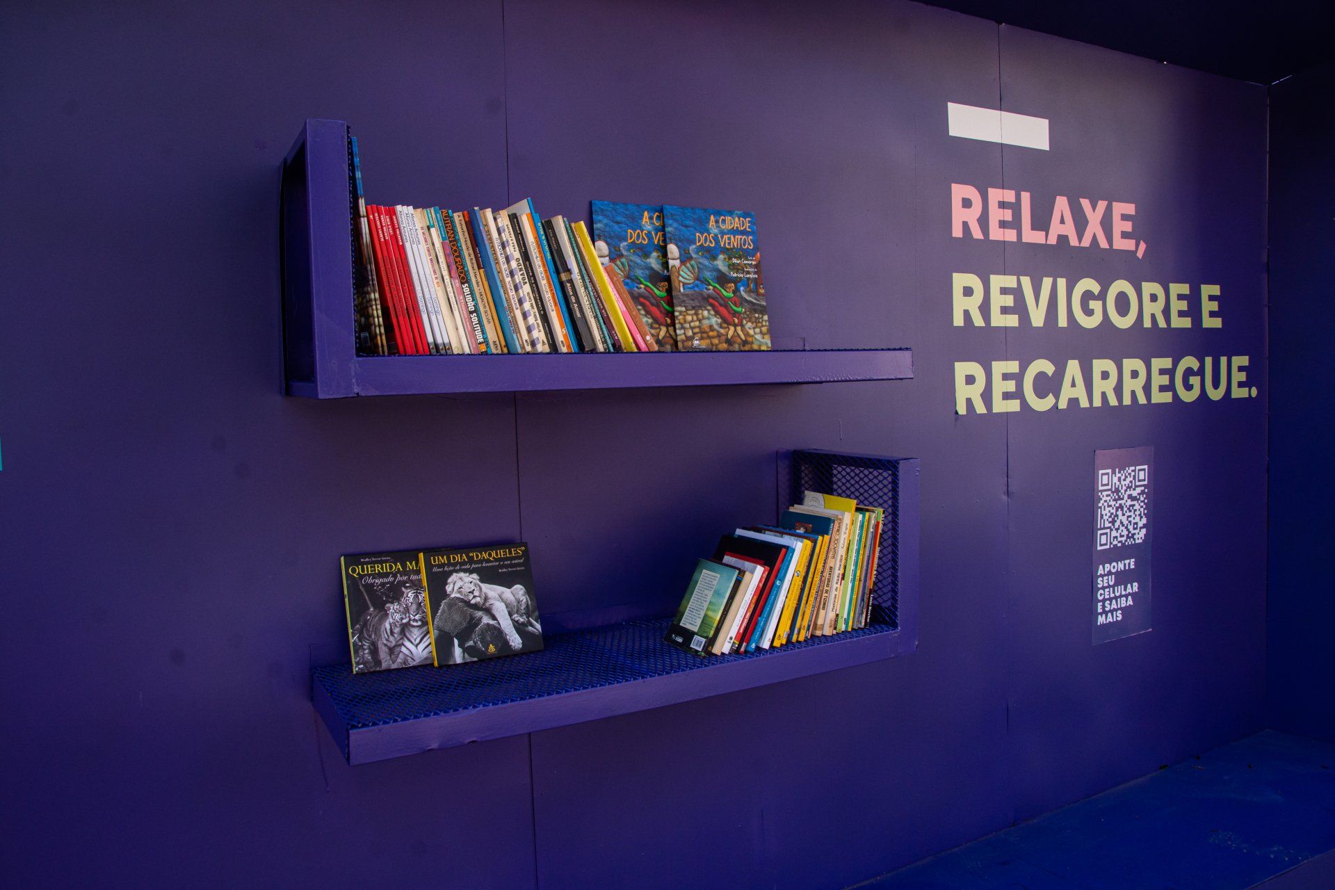 Uma parede roxa com duas prateleiras cheias de livros e uma placa que diz relaxe revigore e recarrega.