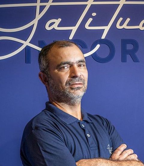 Um homem com barba está parado em frente a uma parede azul com a palavra satisfazer nela