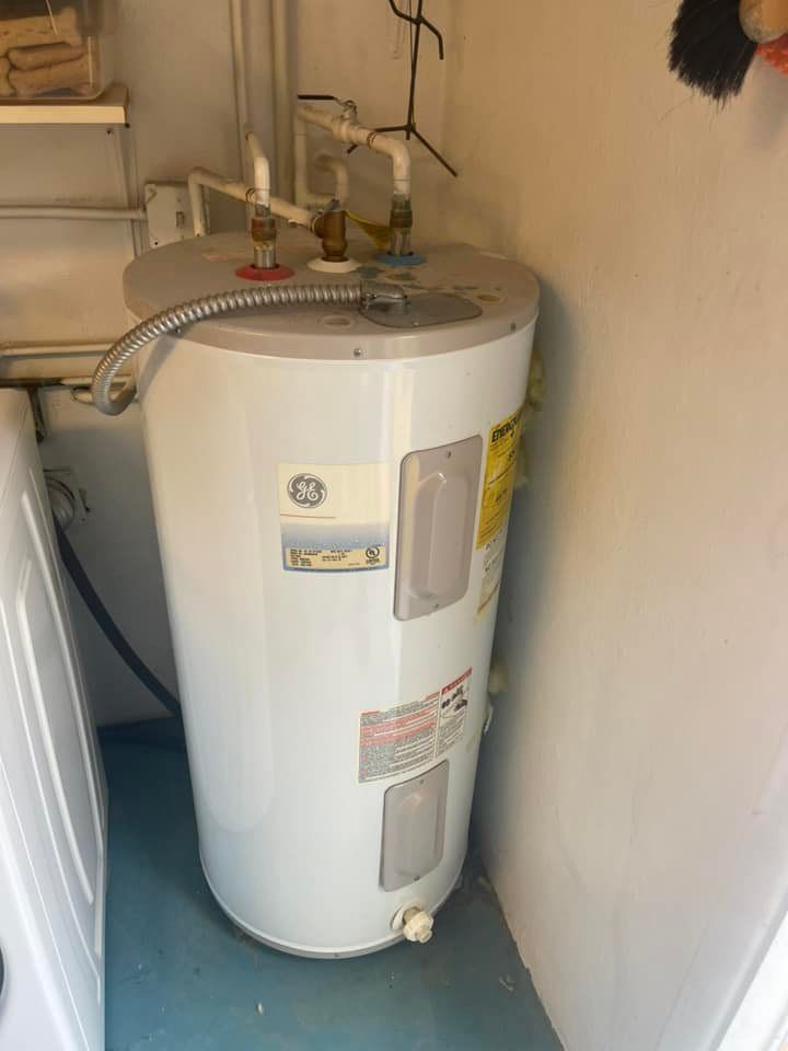 Water heater in a utility closet, white, with various pipes connected.