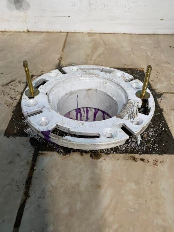 White toilet flange with bolts installed on a gray tile floor, with purple marker stains inside the pipe.