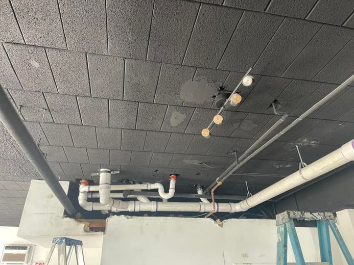 Black-painted ceiling with exposed pipes, plumbing, and lighting fixtures. Construction scene.