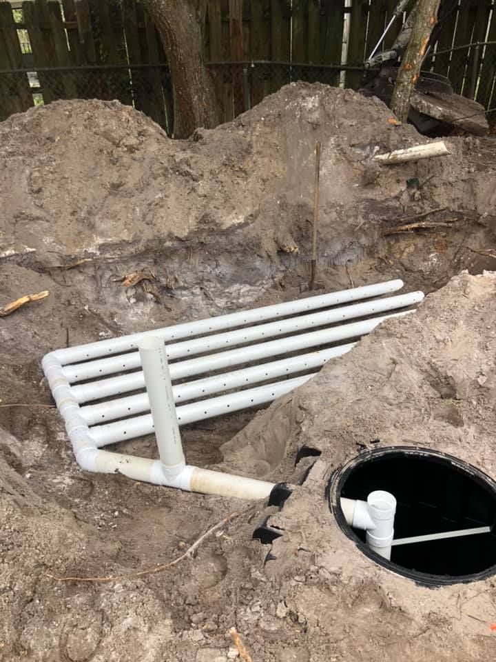 White PVC pipes in a dirt trench, near a manhole cover. Construction site.