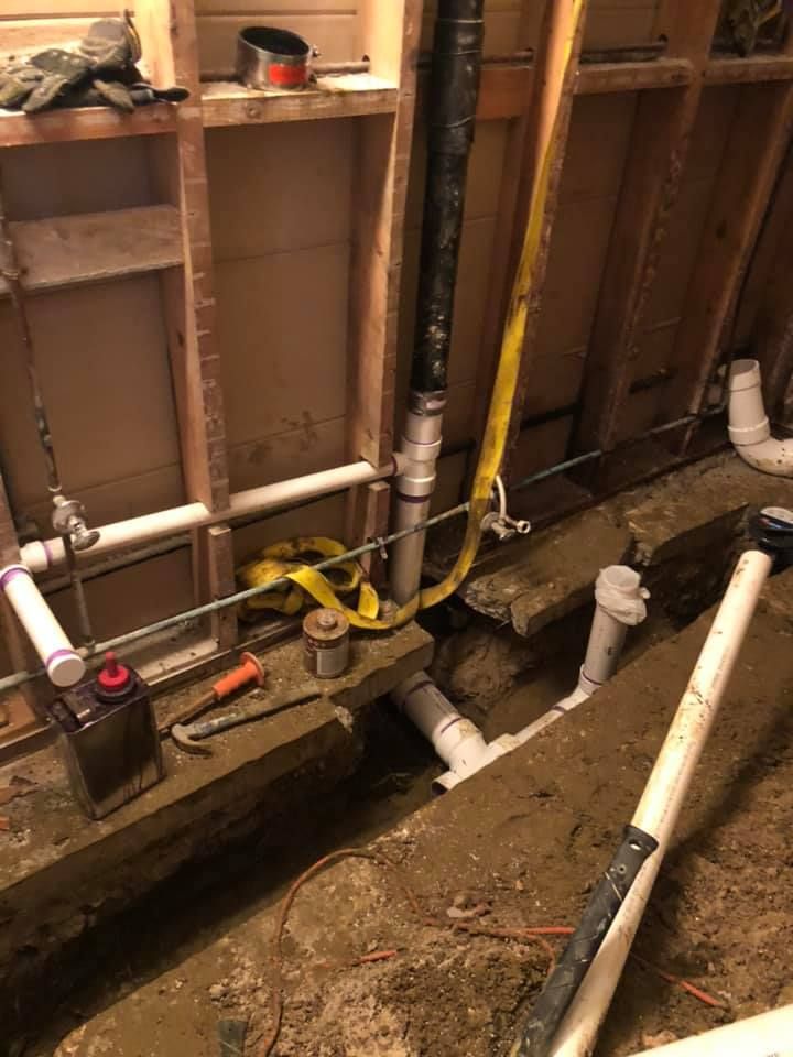 Plumbing work in progress: exposed pipes, trenches, and tools inside a bathroom wall.