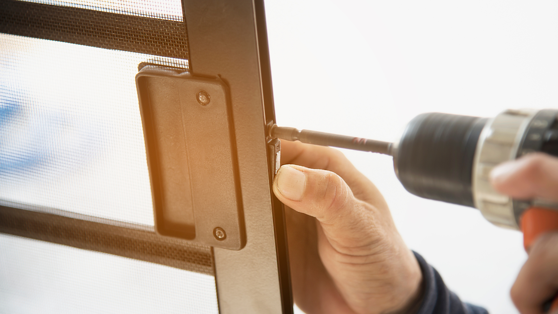 A person using a drill to attach a black latch to a metal frame.