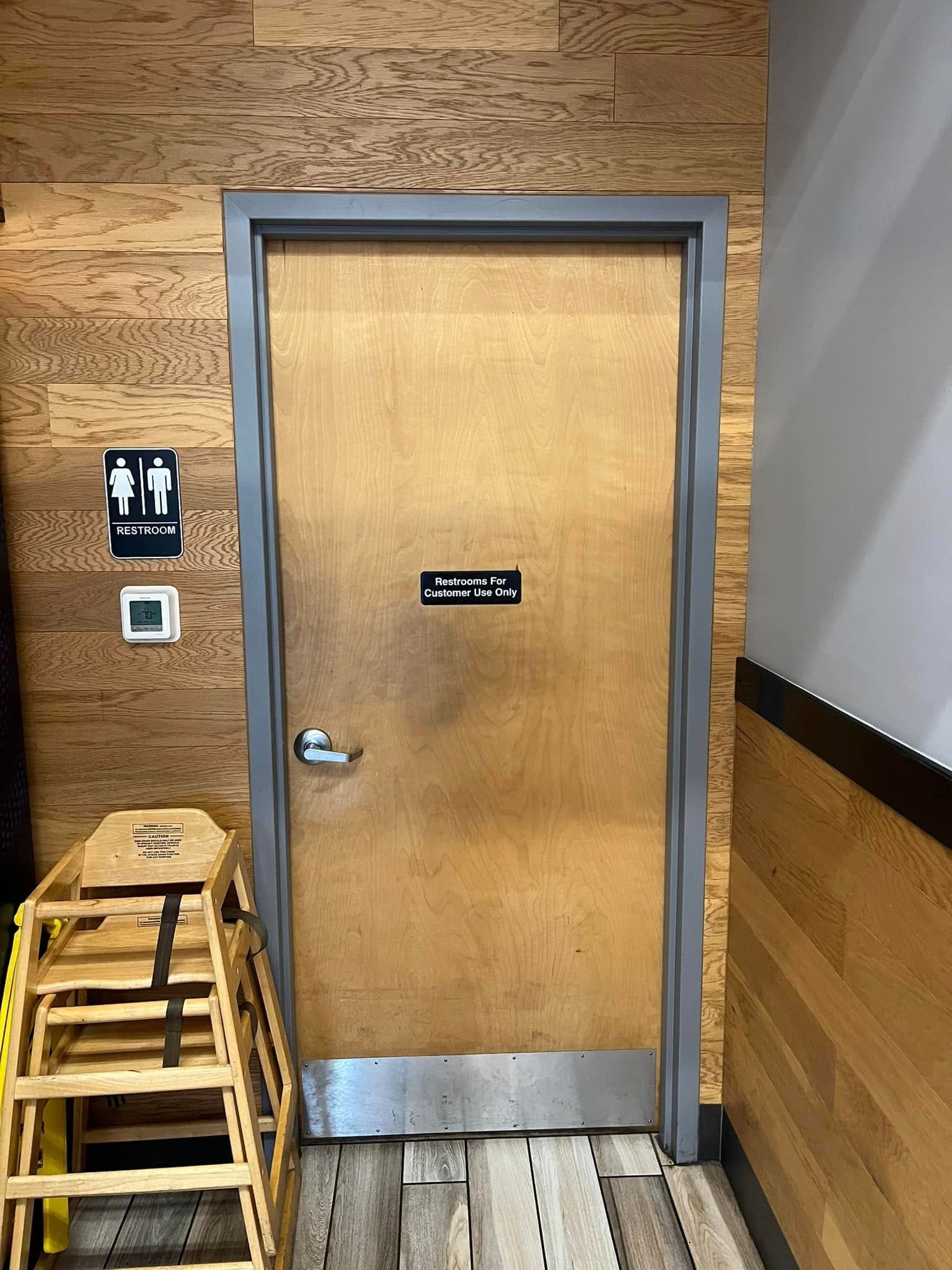 Door with restroom sign and a small sign above, gray frame, wood paneling, small ladder.