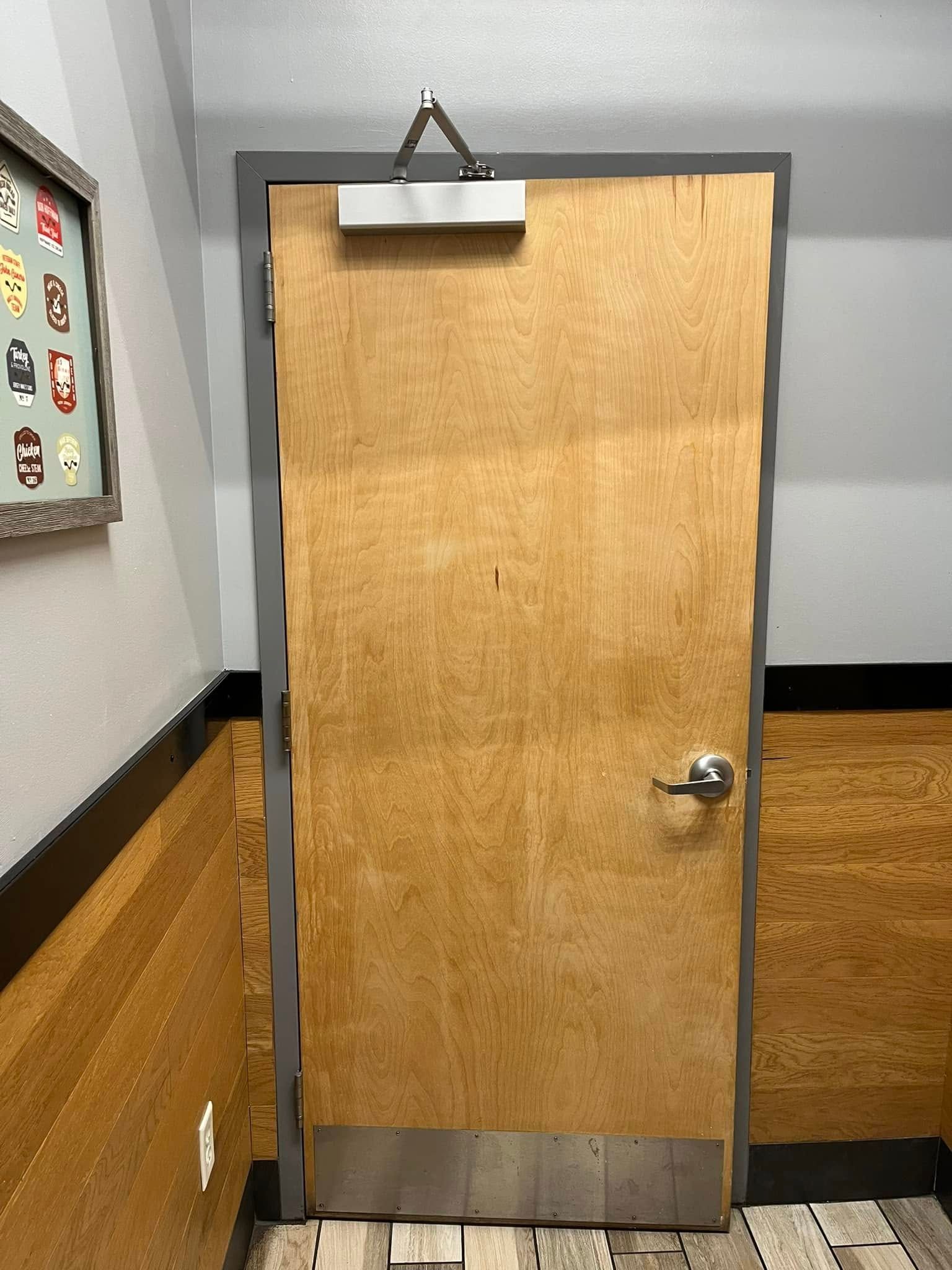 A plain wooden door with a door closer, a silver handle, in a public space.