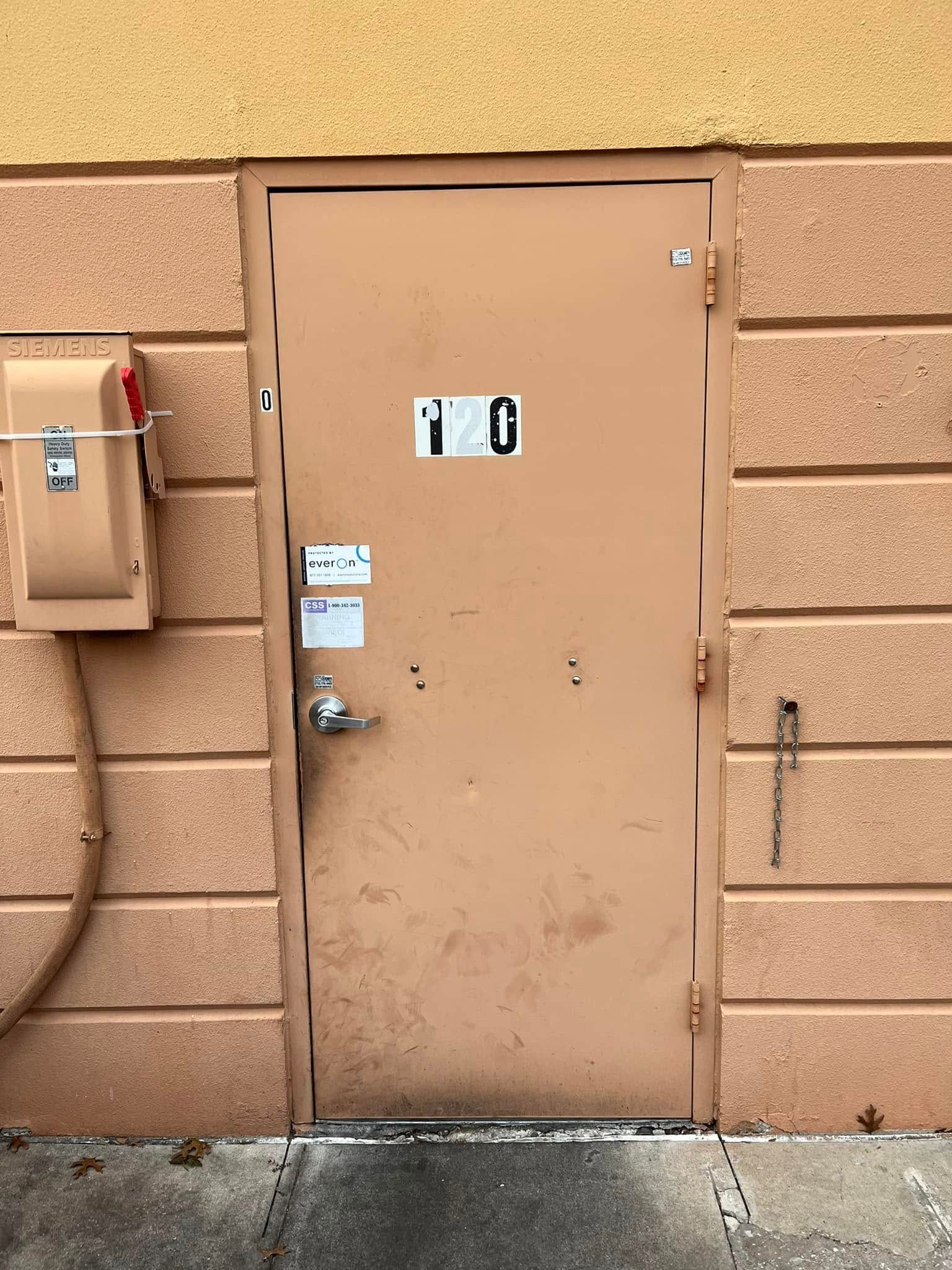 Beige door with stickers, metal handle, and brick wall. A metal box is on the left.