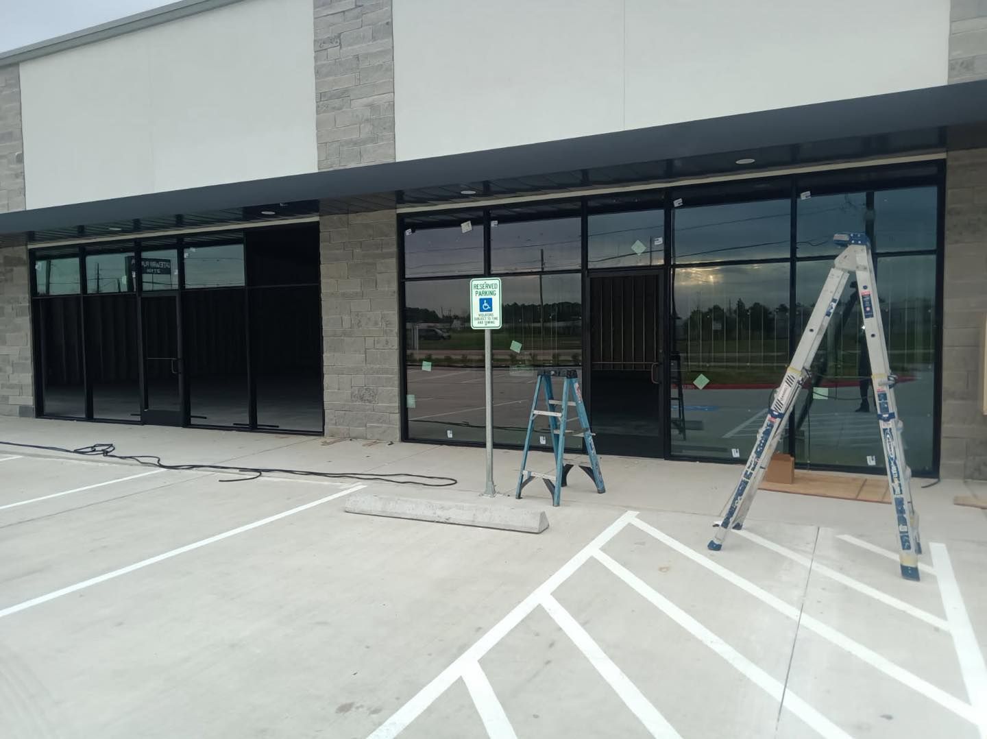 Exterior of a commercial building with black-framed glass windows, construction equipment, and a handicap parking sign.