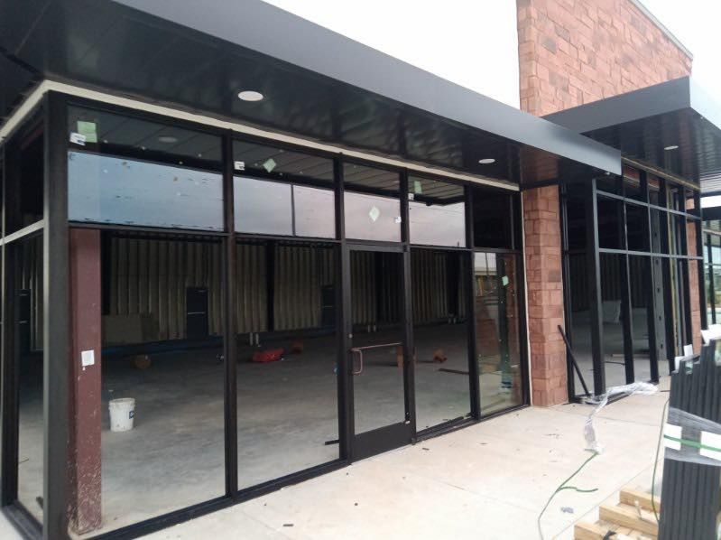 Exterior view of a commercial building under construction with large glass windows and a dark awning.