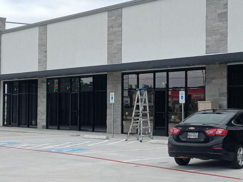 Exterior of a commercial building with black-framed windows, awnings, and a black car parked in front.