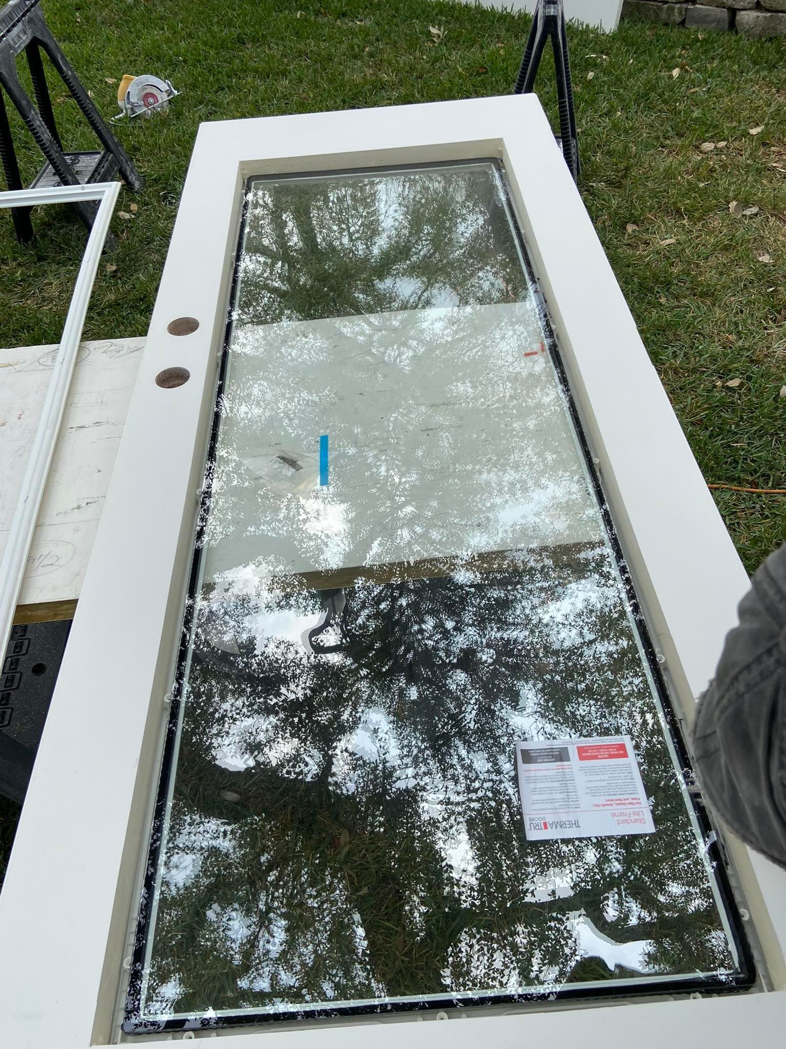 White exterior door with large glass panel, hardware, and attached label, laid on grass.