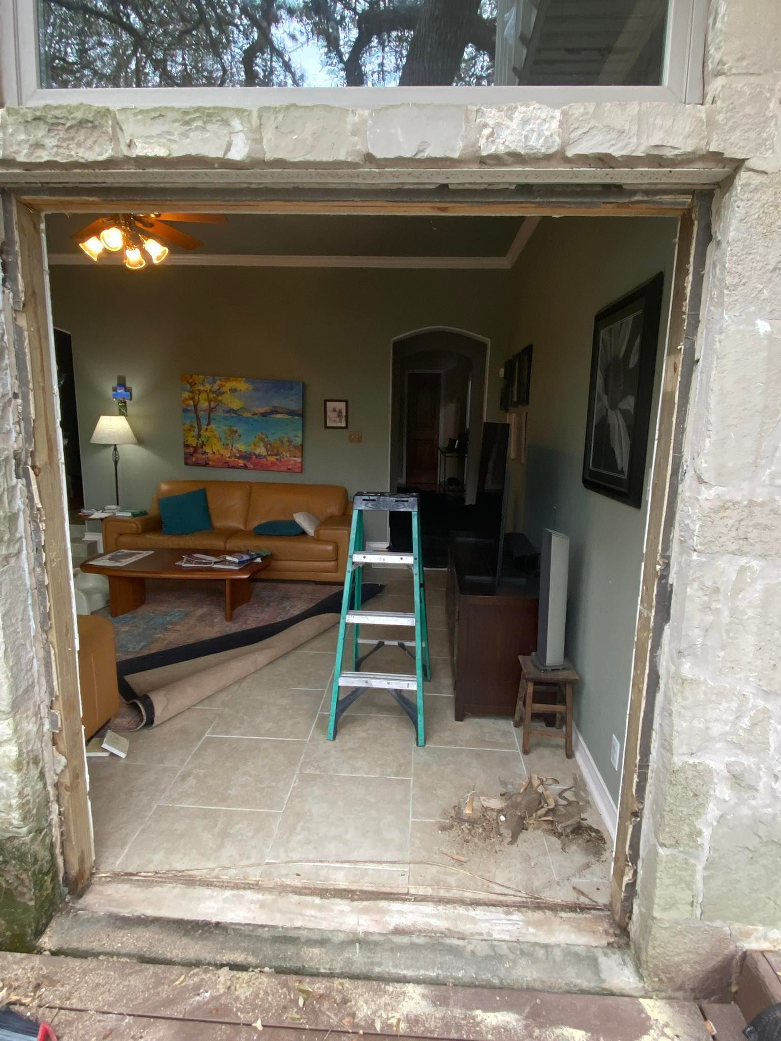 View through an open doorway into a living room with tan couch, art, and a stepladder.