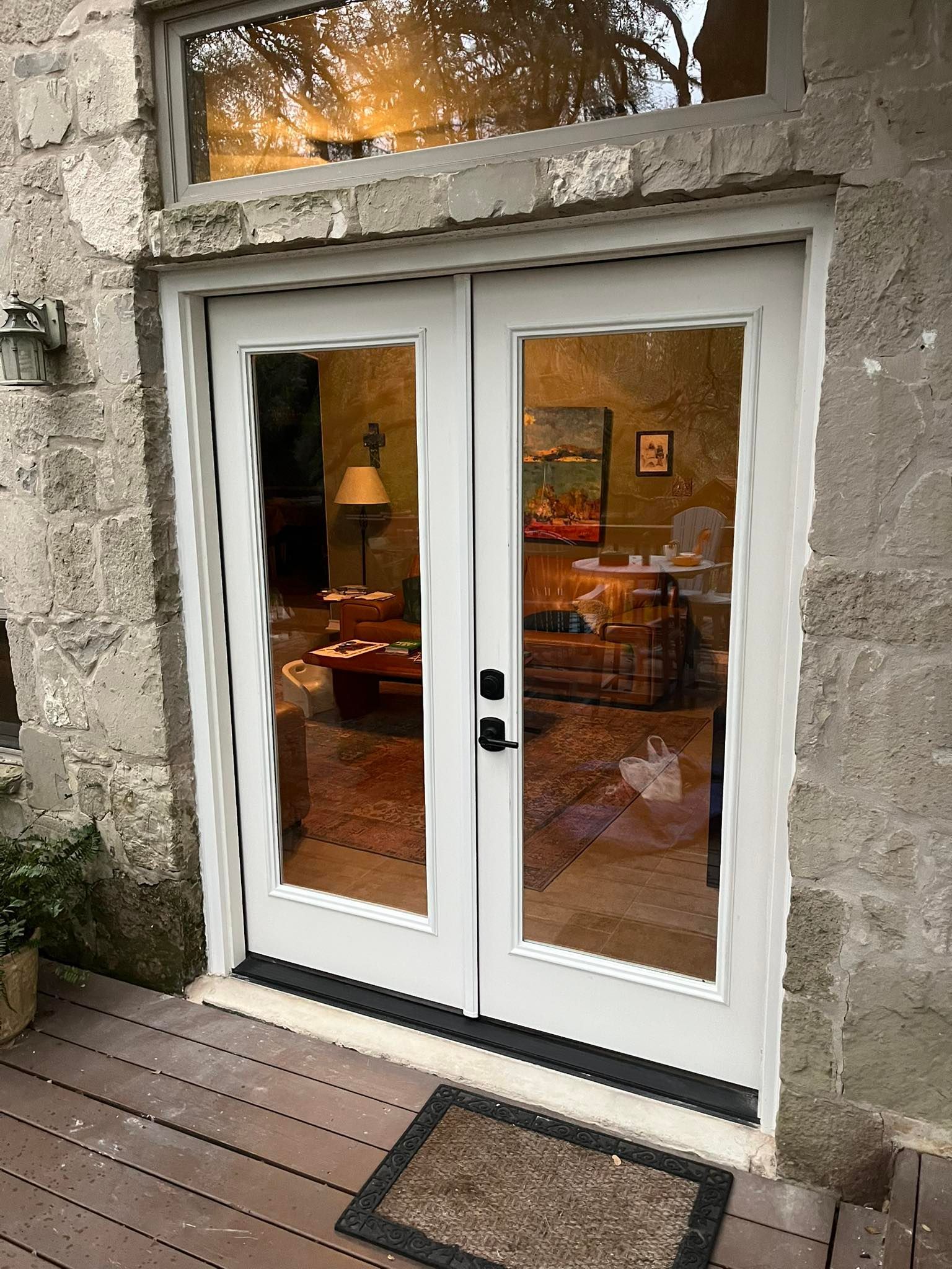 White French doors with glass panes, set in a stone wall, reflecting interior with a table and a painting.