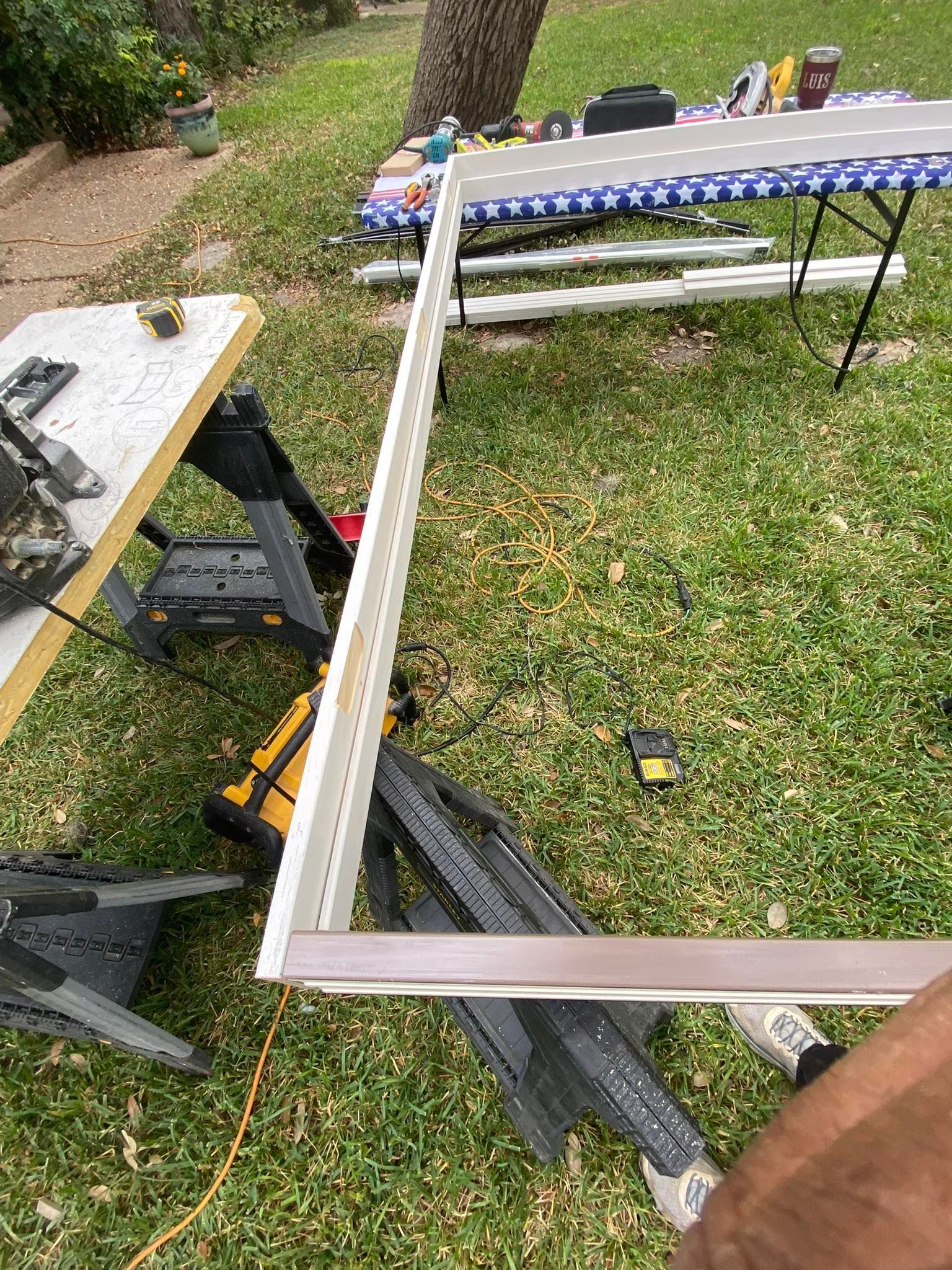 Person building with wood and tools outdoors, green grass, two sawhorses, and a table.