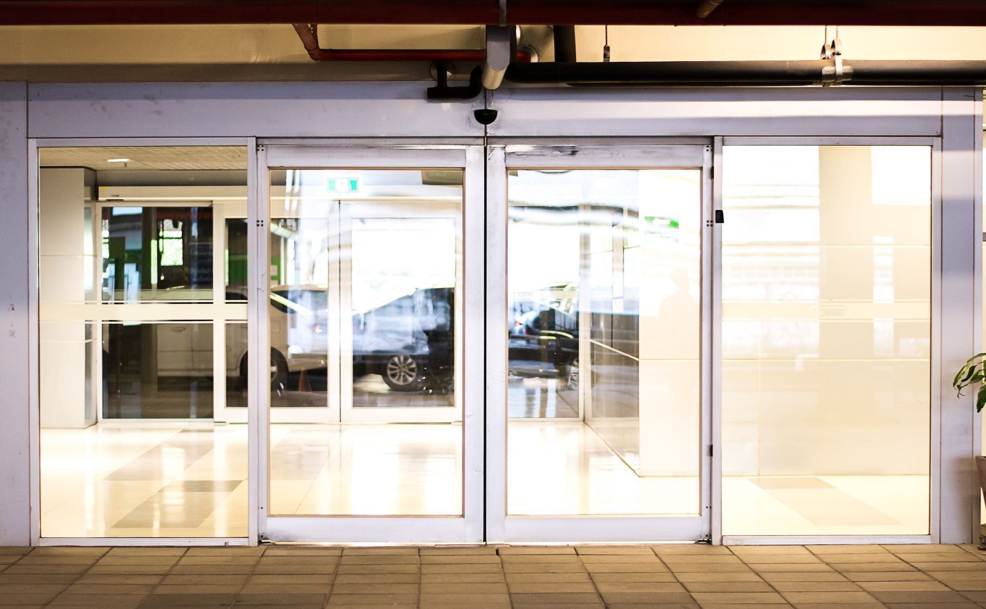 Sliding glass doors of a building entrance, partially open, with interior and exterior views.