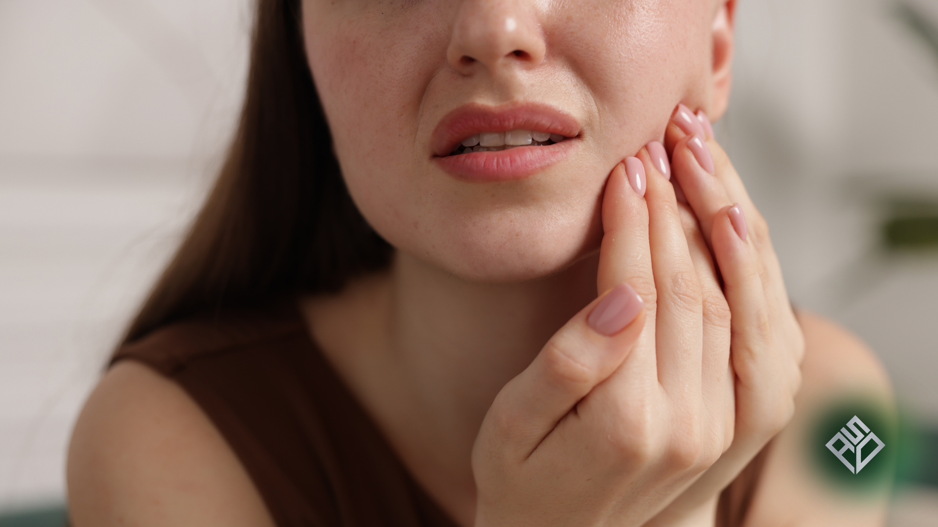 Woman holding face in pain, eyes closed, white tank top, light background.