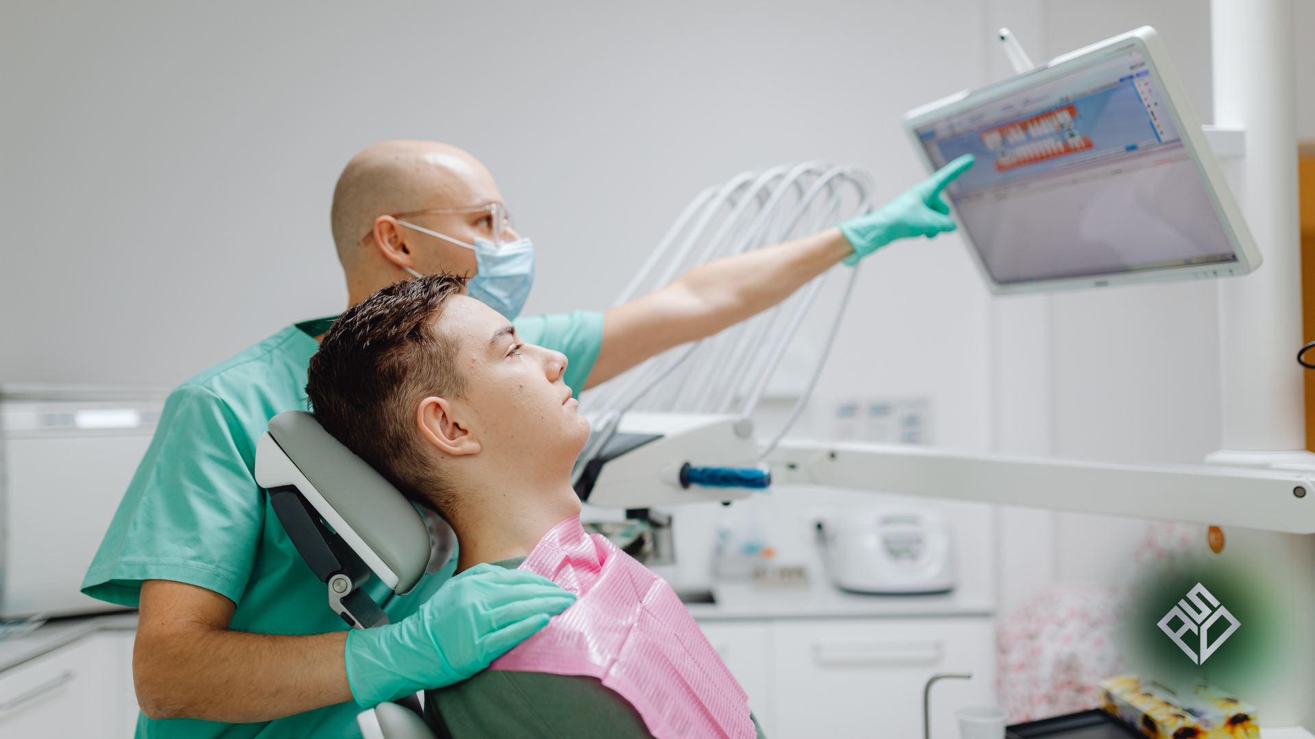Dentist pointing at a digital dental scan on a monitor while the patient sits in the dental chair.