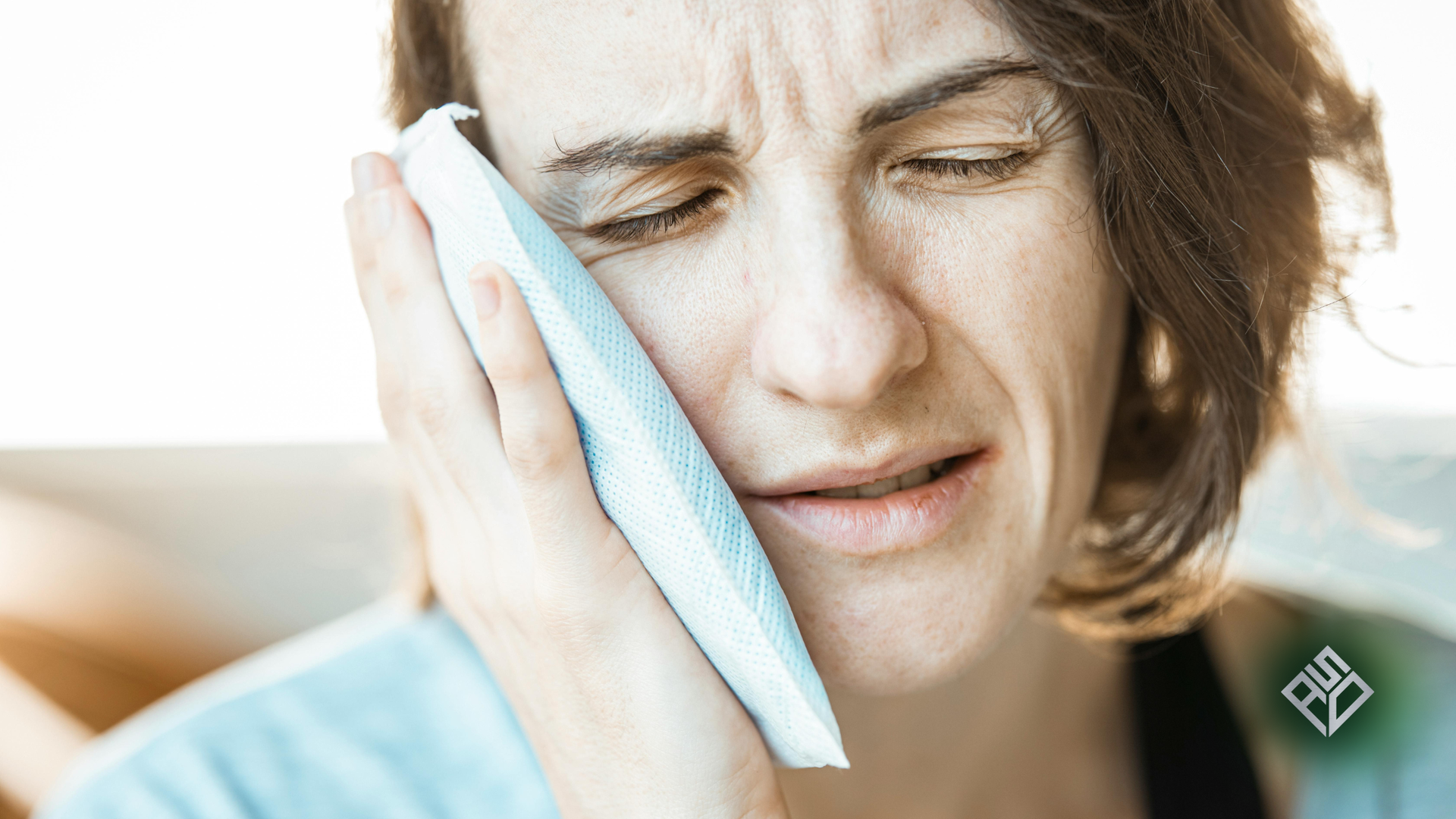 Woman holding ice pack to cheek, grimacing in pain.
