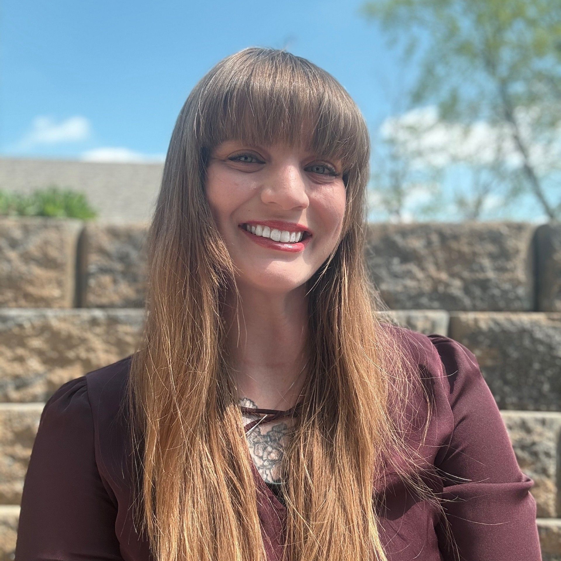A smiling woman outside with a rock wall in background