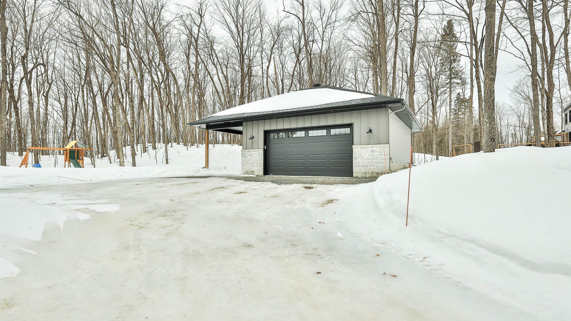 Un garage est recouvert de neige au milieu d'une forêt enneigée.