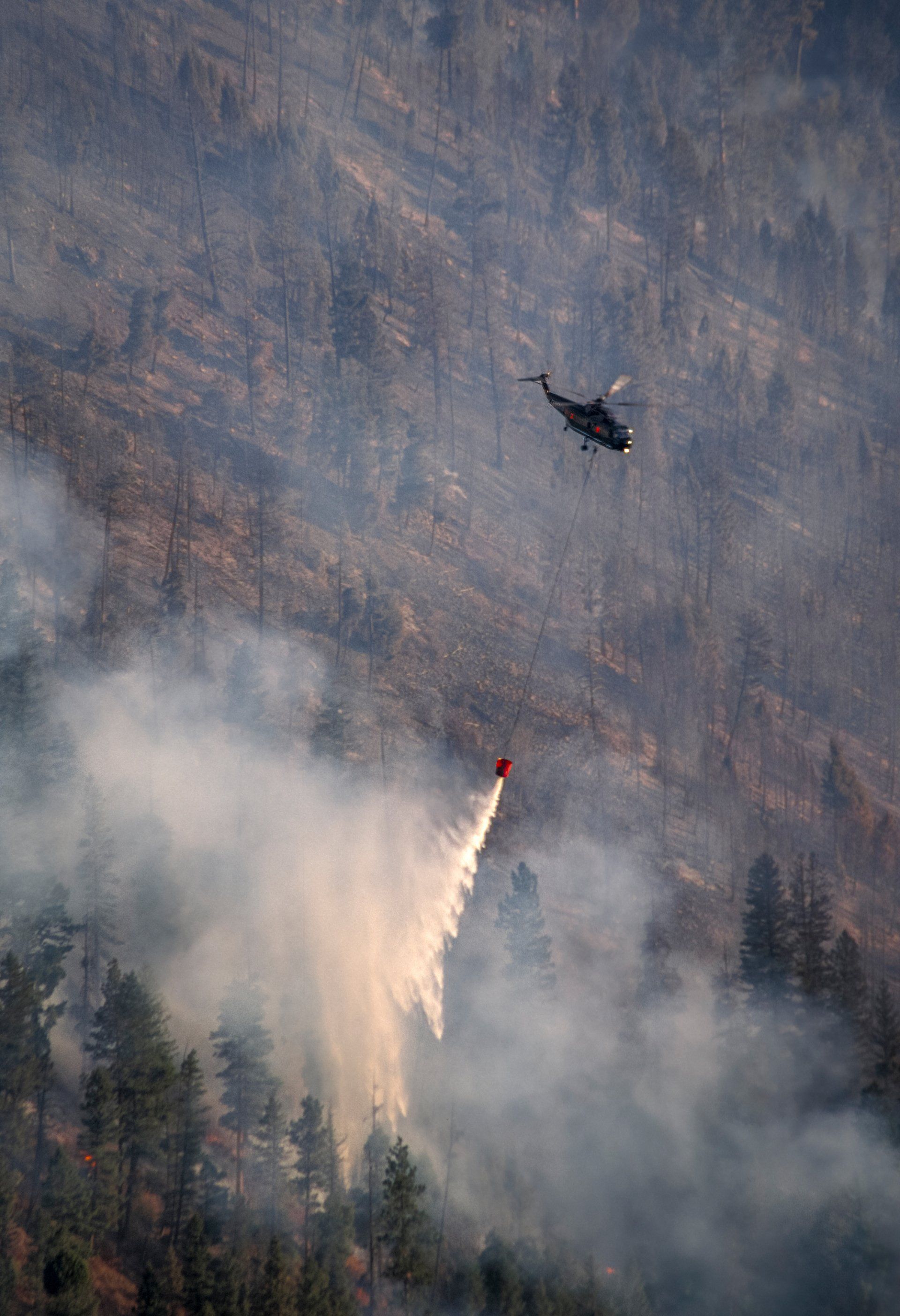 A helicopter makes a late afternoon water drop on the eastern flank of the Bear Fire.