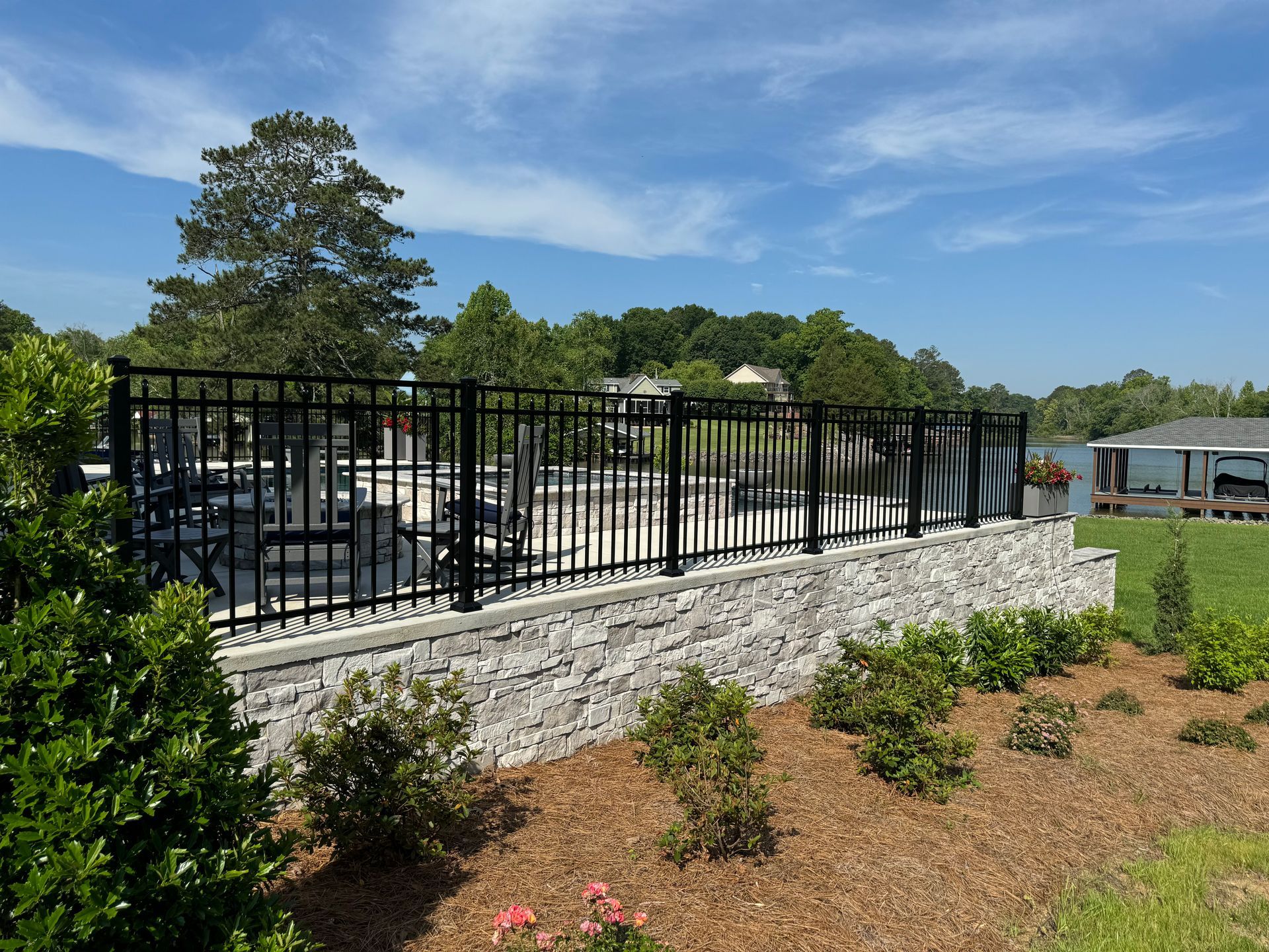 A black fence surrounds a stone wall and a swimming pool.